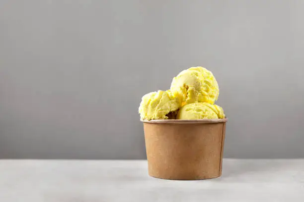 Single paper cup with brigth yellow ice cream balls or scoops against gray background with copy space. Color trends 2021. Zero waste and plastic free concept