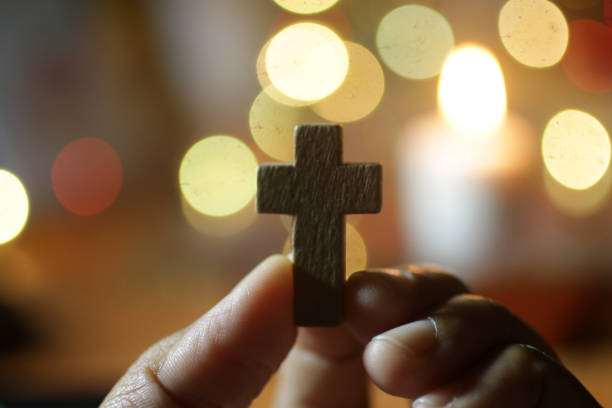 crucifijo de la santa cruz de madera en la mano en el bokeh de oro brillante horneado ligero. - praying human hand worshipper wood fotografías e imágenes de stock