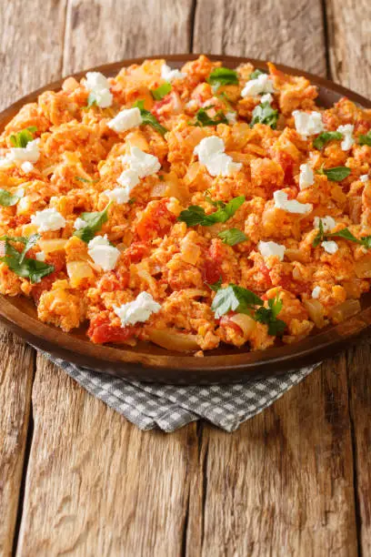 Greek scrambled eggs with tomatoes and feta cheese close-up in a plate on the table. vertical