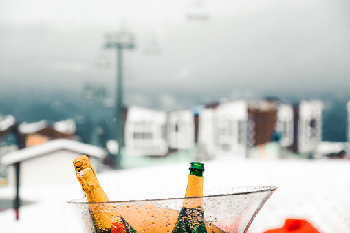 Champagne served in glass bucket in front of beautiful snowy mountain background. Winter holidays in ski resort.