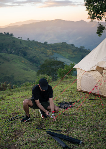 Young man using hammer setting up tent for camping on hill