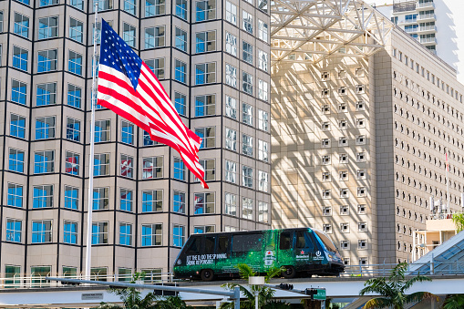 Miami, Florida USA - March 1, 2017: Downtown Miami cityscape with the popular Metromover passing by and a large  American flag flying in the wind.