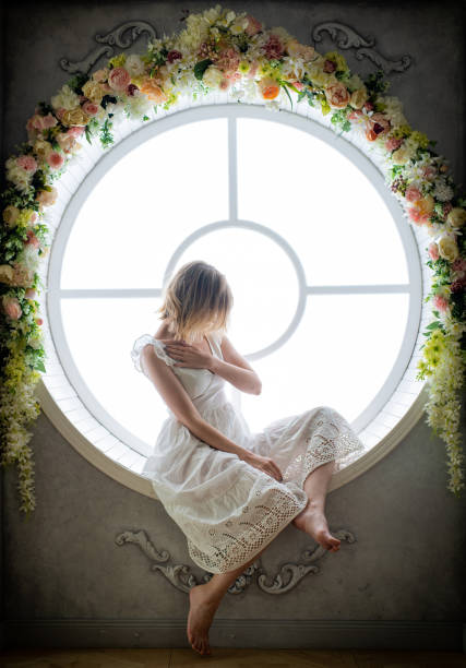 una donna con un vestito bianco di 35-45 anni si siede in una finestra rotonda. distogli lo sguardi. - 40 45 years immagine foto e immagini stock