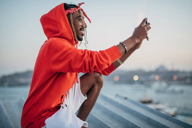 rapper kneeling on the rooftop and taking pictures with smart phone - hip hop urban scene city life black imagens e fotografias de stock