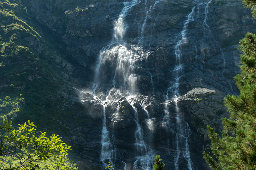 Sunlit water gushes down a steep rocky face into the tranquil waters of Trollfjorden in Lofoten, Norway, framed by lush greenery