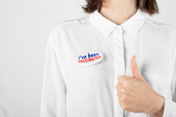 istock Middle age caucasian female model in white blouse with  button pin I've been vaccinated showing thumb up gesture 1291627448
