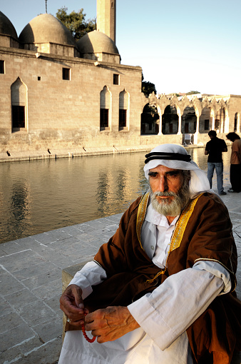 Senior local man, in arabic style clothing, walking near Fish Lake (Balikli Gol), Sanliurfa, Turkey. There is a fish lake in the center of Sanliurfa filled with sacred fish and surrounded by Halil Rahman Mosque. Urfa is a multiethnic city with a Turkish, Kurdish and Arab population.
