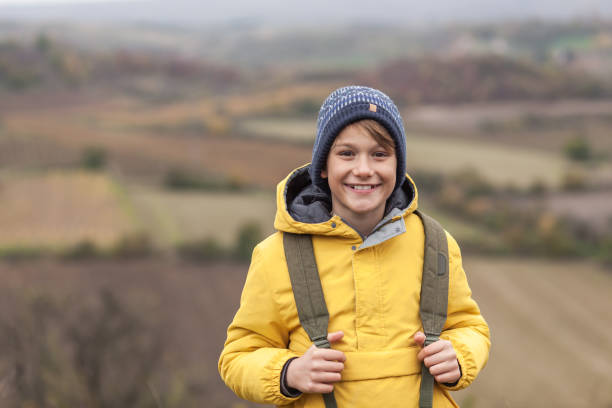 Happy little boy standing in autumn day on a hill and looking at camera. Copy space.