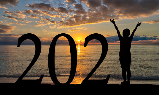New Year 2021 sunrise welcome by the beach with silhouette of woman with raised hands.