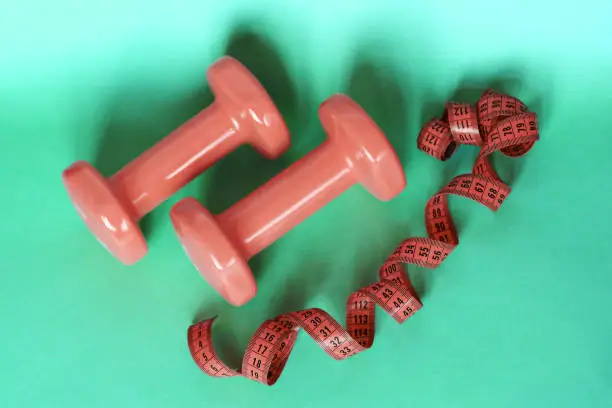 Photo of Pink dumbbells and measure tape on greenery background