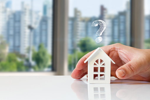 Real estate questions answers concept. Hand shows a house with a question mark on a blurred background.