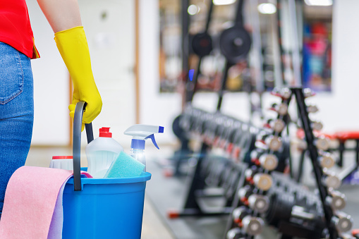 Gym cleaning concept. Cleaning lady stands with a bucket and cleaning products on the background of the gym.