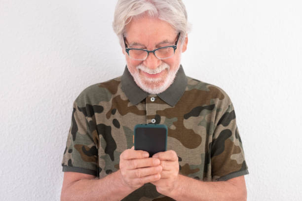 istock Attractive smiling senior man standing against white background using smart phone to send messages. Old people using new technology 1291637091