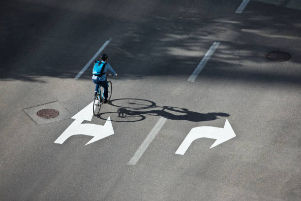 A male bicycle commuter rides a city street on his way to work. He is wearing a bicycle helmet, wears casual clothes, and carries a bicycle messenger style backpack. He rides a fixed-gear or one-speed bicycle.
