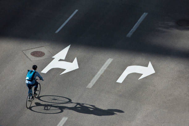 A male bicycle commuter rides a city street on his way to work. He is wearing a bicycle helmet, wears casual clothes, and carries a bicycle messenger style backpack. He rides a fixed-gear or one-speed bicycle.