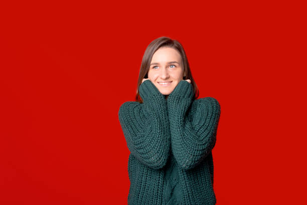 istock Dreaming girl is looking somewhere up while touching her face with hands in sweater. 1291642411