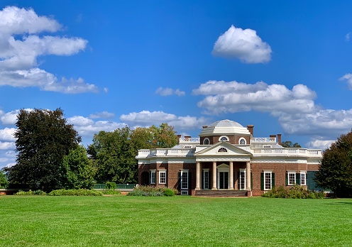 A  view from the back of a large well manicured estate home under clear blue skies in the summer.