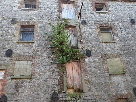 Old docklands stone building, with weeds growing on façade in Drogheda town centre, next to the River Boyne.