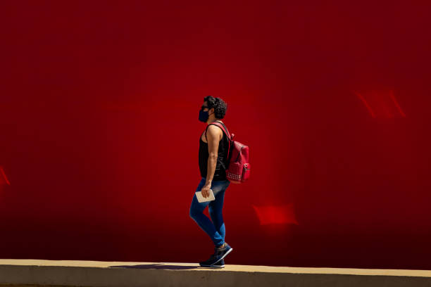 istock Man in mask and backpack walking with a red wall in the background. 1291646473
