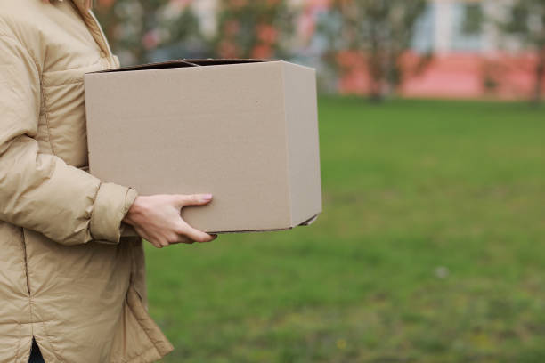 istock Cropped Delivery girl hold empty cardboard box outdoors on a residential complex background. Service coronavirus. Online shopping. mock up. 1291647153