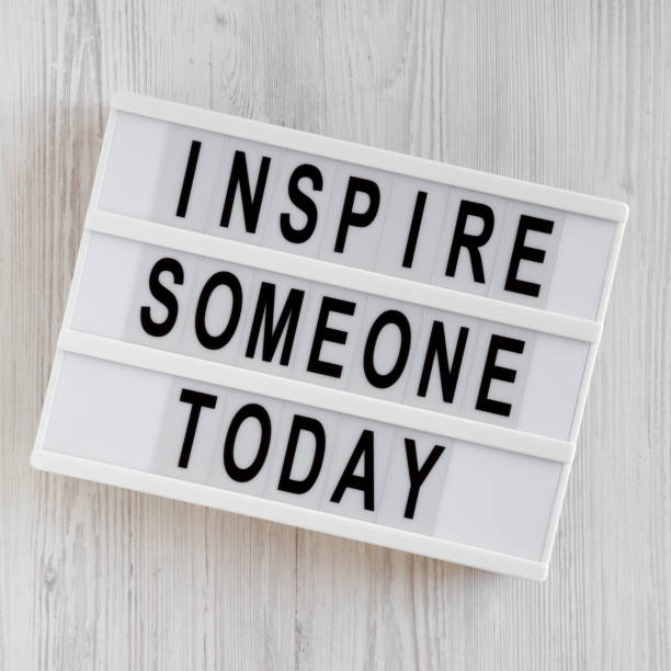'Inspire someone today' words on a lightbox on a white wooden background, top view. Overhead, from above, flat lay.