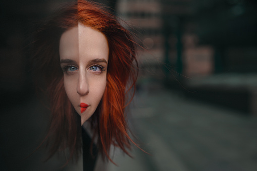 Redhead with blue eyes looking at camera having reflection in glass, bizarre and beautiful