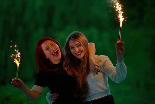 Two women standing outdoors feeling happy during NYE celebration with sparklers and fireworks