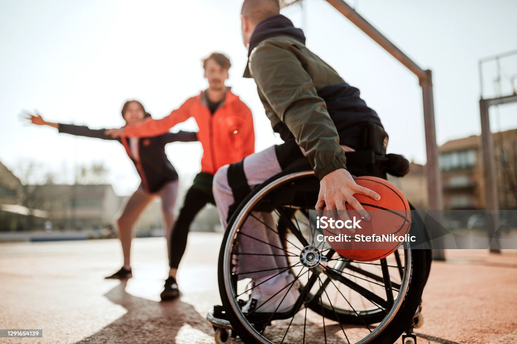 I'm going to win Man in wheelchair playing basketball with friends on sports court Disability Stock Photo
