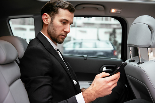 Businessman in the taxi, using a mobile phone. Handsome businessman sitting on the backseat of the car.