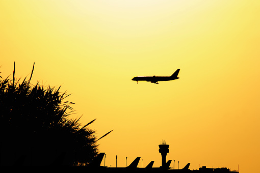 Transportation image of flying commercial passenger airplane over orange colored sunset sky