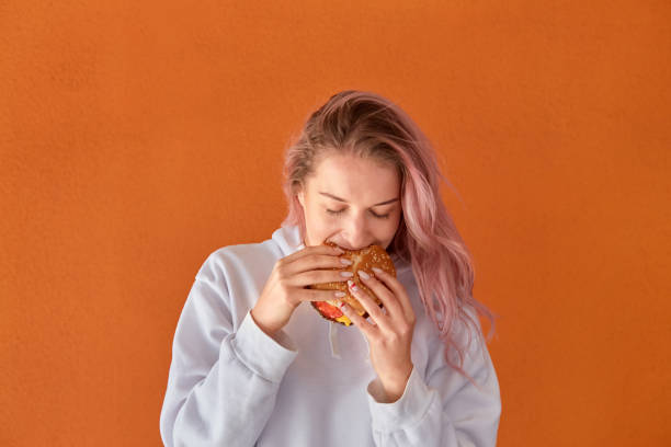 istock A hungry young woman eats a large Burger with an appetite. Orange background. 1291658322