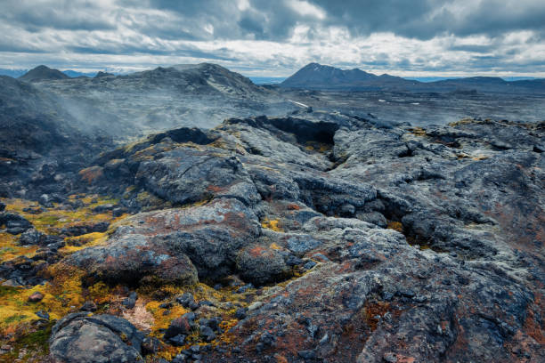 volcanic landscape under dramatic sky on Iceland Volcanic field of rocks under storm clouds with mountains in background on Iceland igneous rock stock pictures, royalty-free photos & images