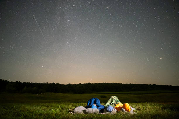 gente descansando en el campo nocturno observando el cielo oscuro con muchas estrellas brillantes. - lluvia de meteoritos fotografías e imágenes de stock