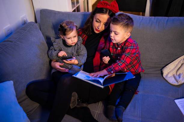 madre leyendo a las hijas cerca del árbol de navidad. foto de stock - 18 23 meses fotografías e imágenes de stock
