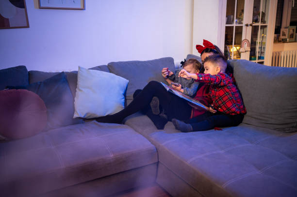 madre leyendo a las hijas cerca del árbol de navidad. foto de stock - 18 23 meses fotografías e imágenes de stock