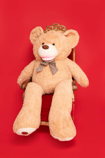 istock Big teddy bear sitting on christmas chair, red studio background. 1291681162