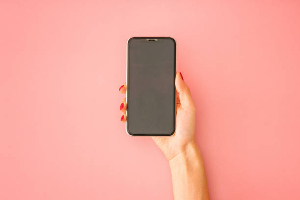 istock Woman hand holding smartphone on pink background. Empty place for text on black screen 1291681946