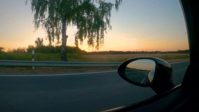 CLOSE UP: Scenic view of golden-lit countryside from the window of moving car
