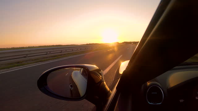 CLOSE UP Summer evening sun rays shine on a sportscar driving down empty freeway