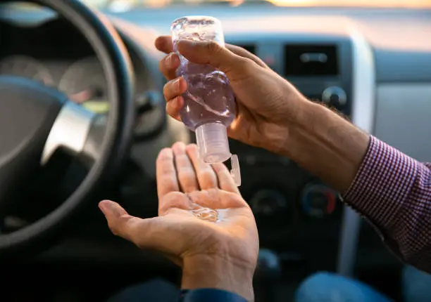 Close up of a man applying sanitizer gel to her hands inside his car