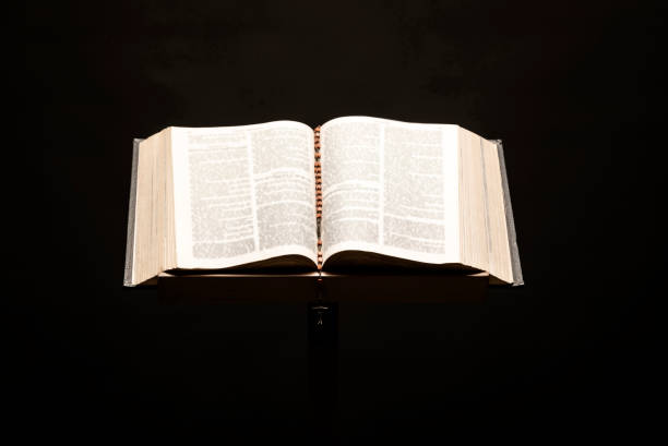 istock Holy Bible open on pedestal on black background 1291692303