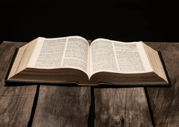 istock Holy Bible open on pedestal on black background 1291692385
