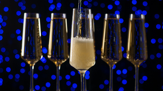Filling a glass with bubbling sparkling wine on a blue background. A popular alcoholic drink.