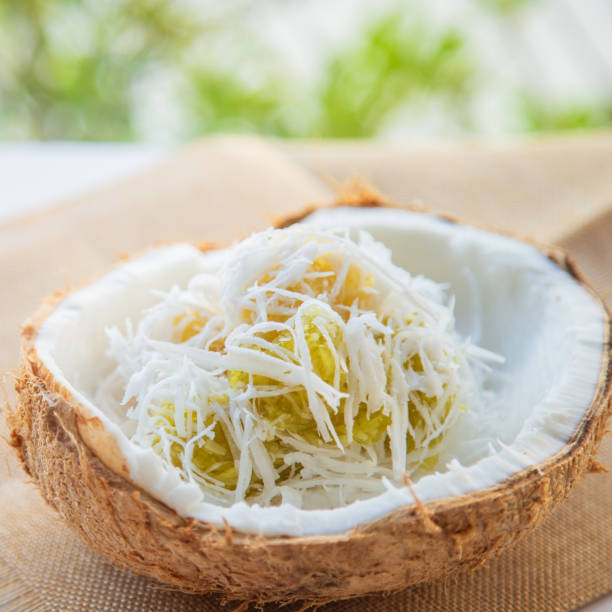 Thai dessert homemade steamed cassava cake with a fresh coconut in a coconut shell with pandan leaves blurred background on white table.