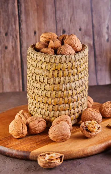 Photo of Walnuts in a wicker basket, whole and finely chopped, next to the filling and shells on a wooden background. Home storage of winter preparations