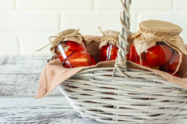 los tomates caseros se conservan en frascos de vidrio en cesta de mimbre blanco sobre fondo de madera - basket wicker marinated preserves fotografías e imágenes de stock