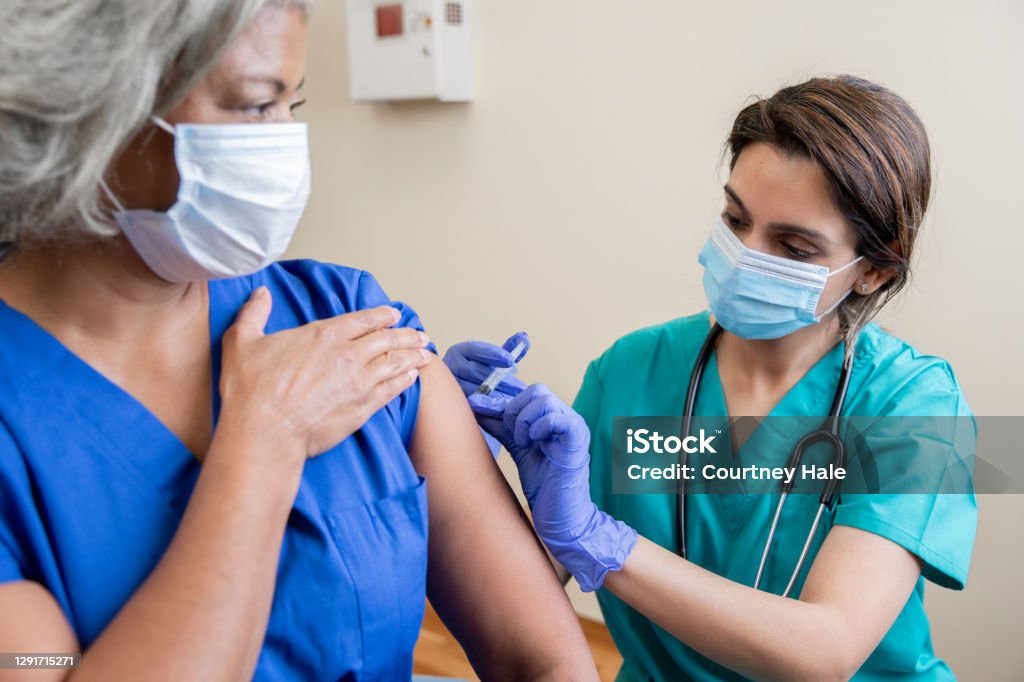Nurse gives senior adult healthcare worker the Covid-19 vaccine Vaccination Stock Photo