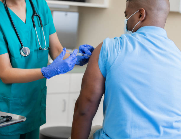 медсестра дает зрелый афроамериканец вакцинацию в кабинете врача во время пандемии коронавируса - doctor medical injection female general practitioner стоковые фото и изображения
