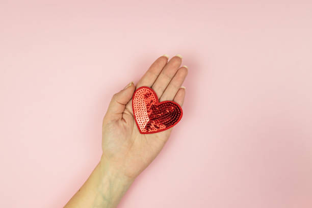 istock Female hand holding red sequin heart on pink background. Creative minimal layout with copy space 1291716869