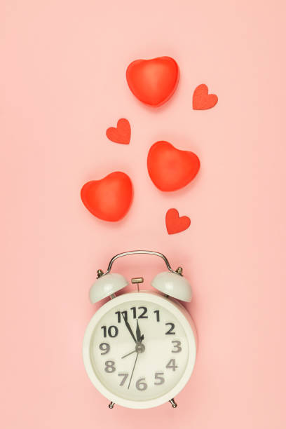 istock Pink Background with white alarm clock and red hearts. Creative layout. Top view. Time for love and greetings. 1291716872